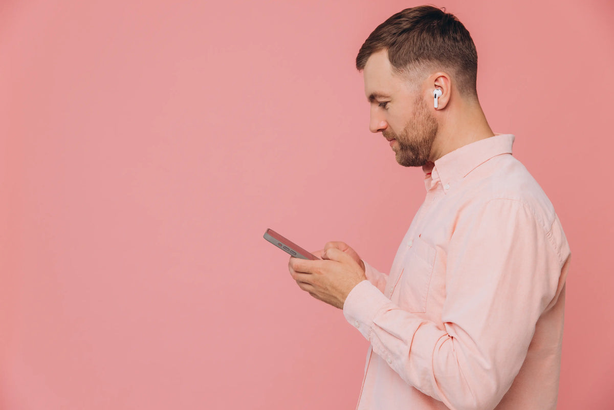 Man using phone standing infront of pink background | What Does a 2-Year Warranty Really Mean When Buying Pre-Owned?