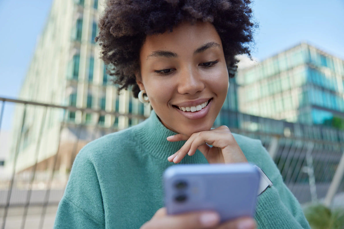 Lady smiling at iPhone | Why a Pre-Owned iPhone Makes Sense in 2026